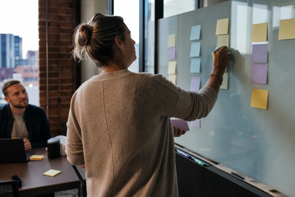 In-house talent lead arranging interview loop notes on a glass wall in a small tech office