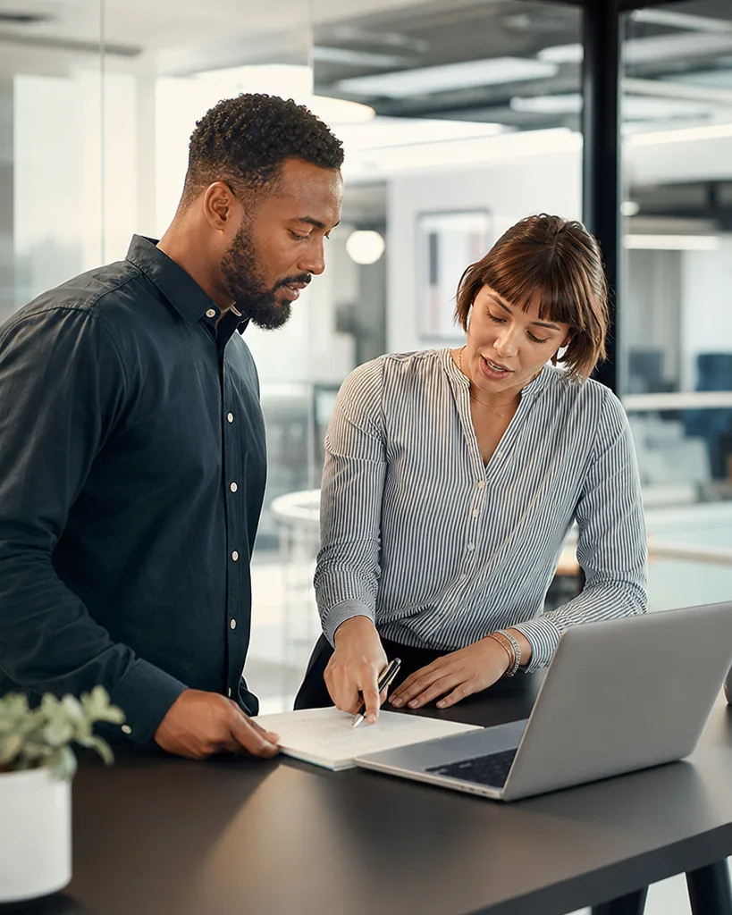 Two startup colleagues comparing software costs at a standing desk with a notepad